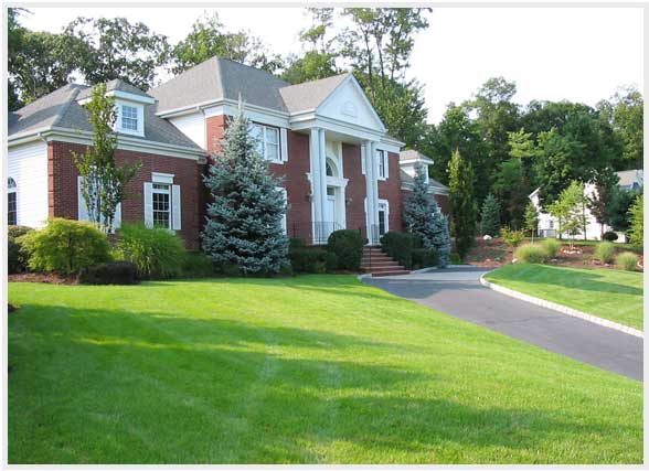 Thick green lawn in front of a two-story brick home kept on a recurring Augusta lawn care plan
